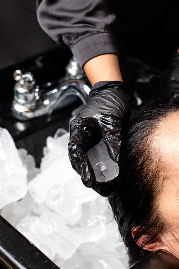 Estilista pasa un cubo de hielo por el cuero cabelludo de una clienta