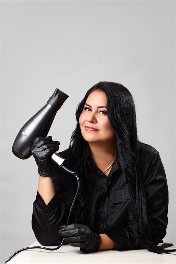 Estilista de cabello con guantes negros posa con un secador