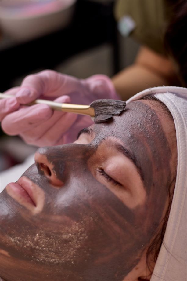 Cosmetóloga con guantes rosados aplica mascarilla con brocha