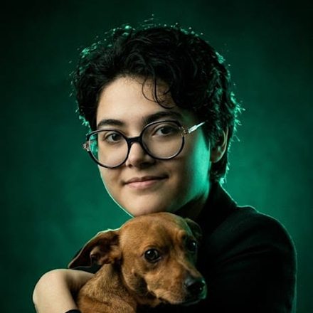 Ana con lentes, abrazando a su perrito sobre fondo verde