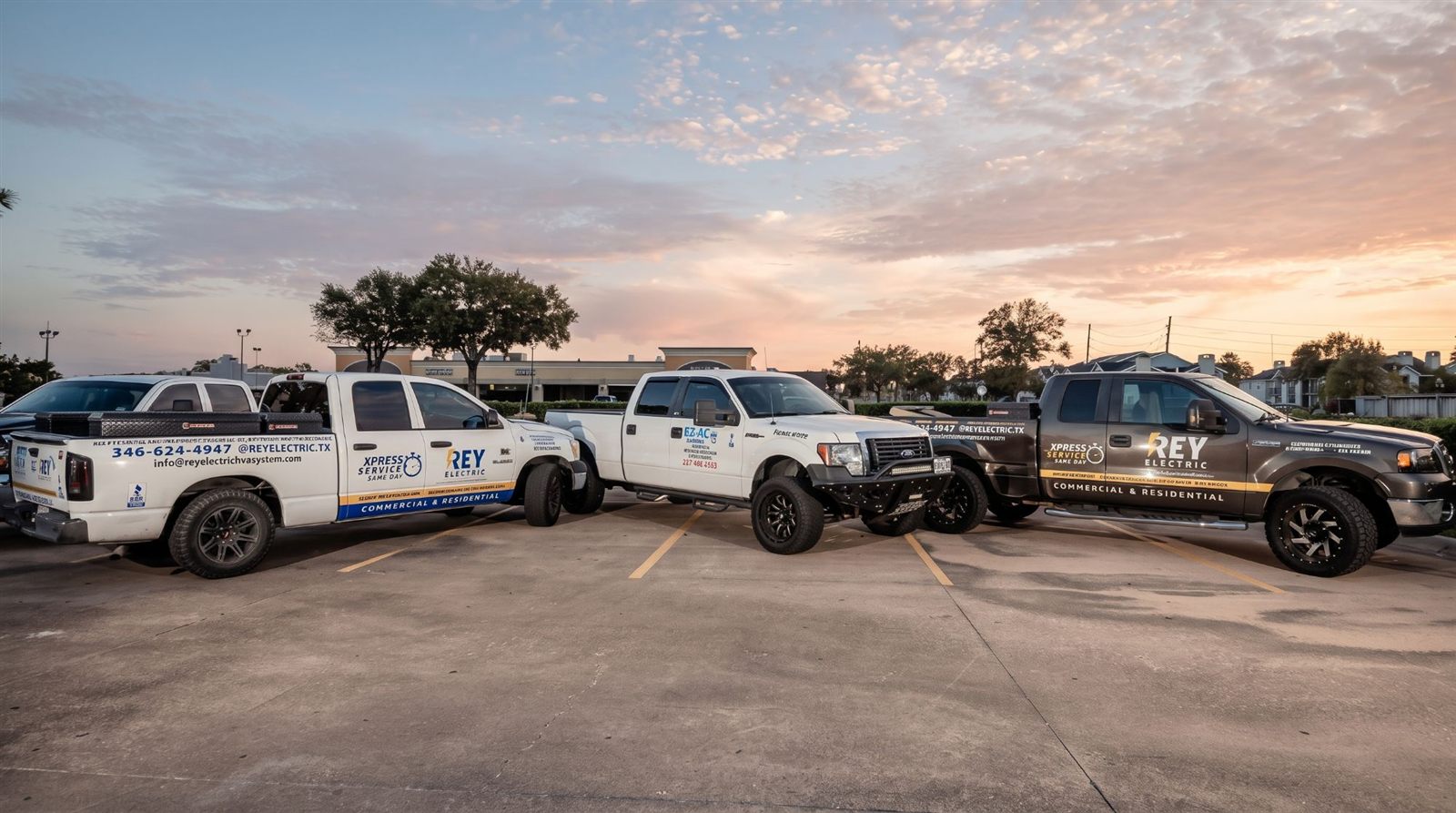 Tres camionetas rotuladas de Rey Electric estacionadas al atardecer